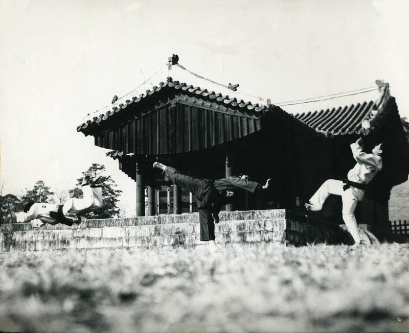 Hwa Rang Do® Founder Supreme Grandmaster Dr. Joo Bang Lee demonstrating a palm back kick against two opponents during Master’s Outdoor Training, Seoul, Korea 1960s