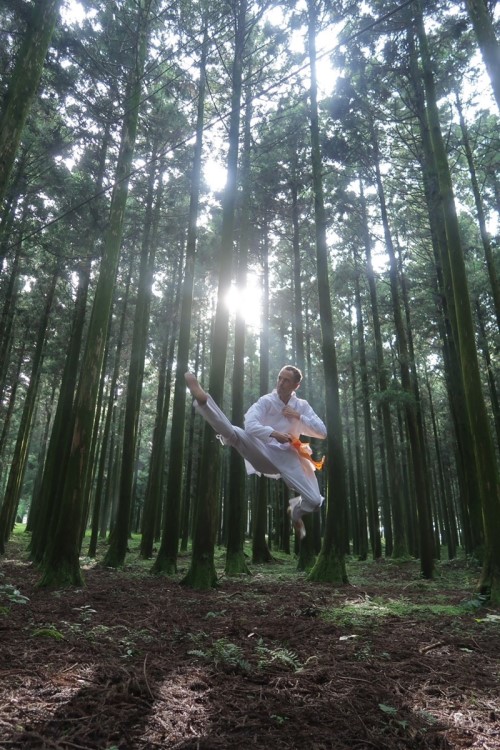Photo 1 : Coup de pied vrillé & sauté dans une forêt de cèdres japonais de Jeju en « cheollik » (manteau de la période Goryeo) ⓒ Maître Jean-Sébastien Bressy