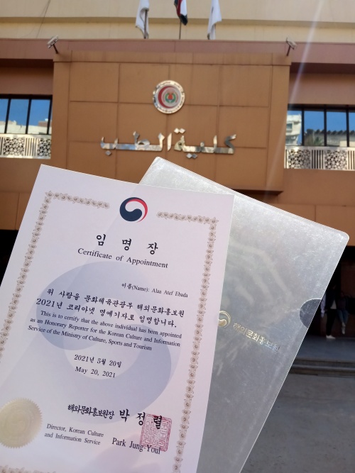 شهادة تعييني لعام ٢٠٢١ كمراسلة فخرية لكوريا.نت، من أمام مبنى جامعتي، كلية الطب جامعة المنصورة. (الصورة من آلاء عاطف)