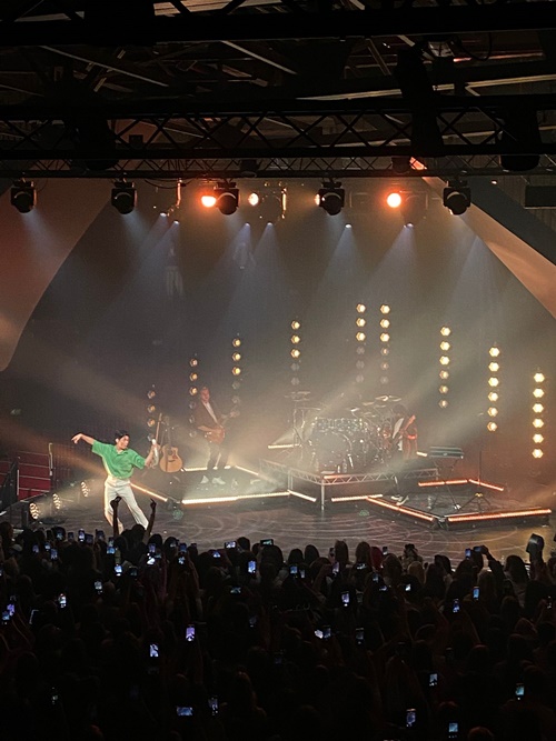 Eric Nam fait un geste gracieux du bras droit en tenant son micro dans l’autre main © Molly Bai