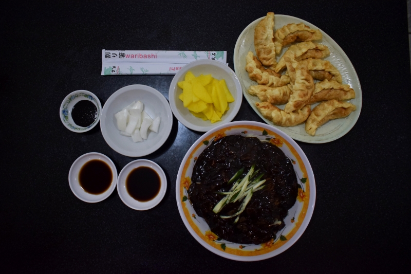 He probado unos fideos con salsa negra y empanadas coreanas de carne picante con salsa de soja y vinagre, junto con pedazos de nabo en vinagre y cebolla cruda.