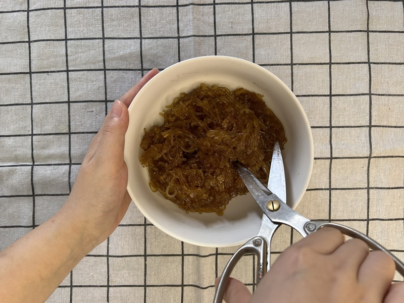 Miến sau khi được trộn chung với gia vị thì dùng kéo cắt nhỏ sợi miến. (Ảnh: Lưu Hoàng Nhi)