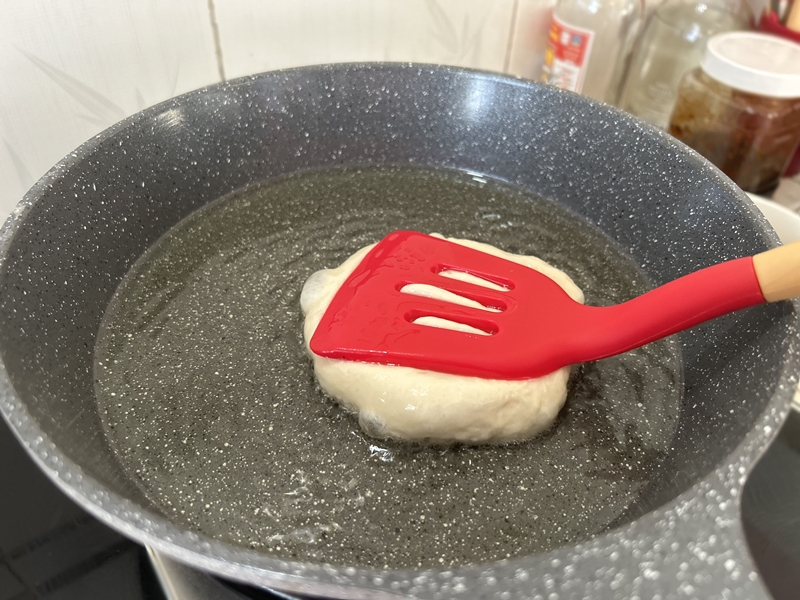 Dùng phới để nhấn bánh dẹt phẳng ra. (Ảnh: Lưu Hoàng Nhi)