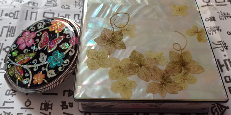 La foto muestra el espejo (izda.) diseñado con flores y mariposas de lacado y el bloc de notas hecho con flores secas utilizando lacados de nácar. 