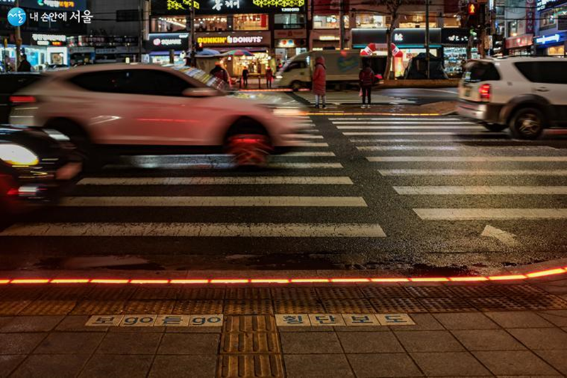 Los peatones esperan para cruzar la calle, mientras se observa el semáforo en el suelo con la luz en rojo. | Gobierno Metropolitano de Seúl 