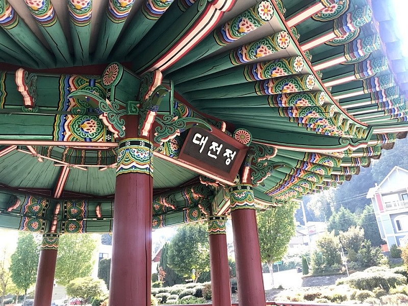 La foto muestra la placa con el nombre del pabellón, mientras los detalles de las pinturas en el techo al estilo dancheong destacan. | Con sulado General de la República de Corea en Seattle