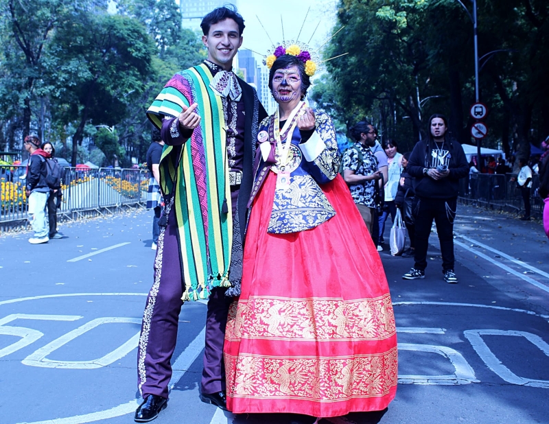 La líder del contingente y el embajador lucen trajes tradicionales de México y Corea, simbolizando la unión cultural en este evento.