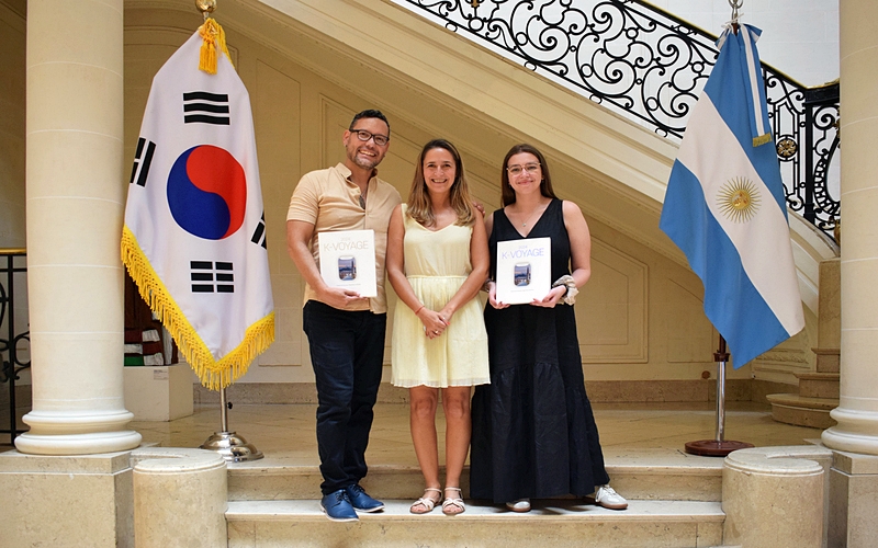 Los reporteros honorarios Florencia Vaineras (derecha) y José Alirio Peña (izquierda) posan con el libro 'K-Voyage' con Eliana Gissara, responsable de Comunicaciones del Centro Cultural Coreano en Argentina. | Juan José Díaz