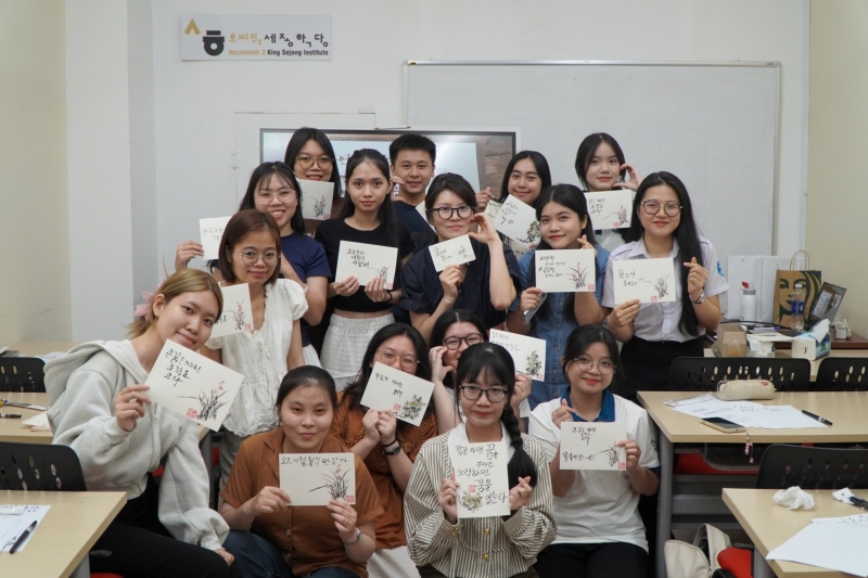 Các bạn học viên cùng hoàn thành tác phẩm thư pháp của mình trong buổi học “K-Calligraphy - Thể hiện câu chuyện của bạn qua tiếng Hàn” với sự hướng dẫn tận tình của cô giáo Lee Yu In (người ở giữa, áo đen và đeo kính). (Ảnh: Học viện King Sejong Hồ Chí Minh 2)