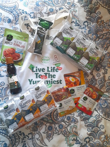 En la imagen, algunos de los obsequios entregados a los participantes: una bolsa reutilizable de tela con un broche de Cuisine.K y, en su interior, productos como algas saladas, algas con sabor a wasabi, aceite de sésamo, algas con sabor a aceite de sésamo, salsa clásica para bulgogi, salsa para tteokbokki y salsa picante para bulgogi. | Celia Algaba