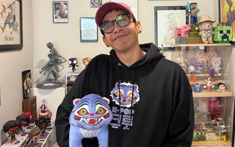 Cruz Contreras, en su espacio de trabajo sosteniendo un peluche de la película 'Las guerreras K-pop' y en el fondo se pueden ver recuerdos de algunas películas en las que ha participado.